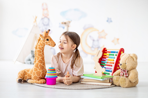 a small child girl playing with toys on a mat in a bright nursery or a playroom lying on the floor, a smiling child at home playing, early preschool development.