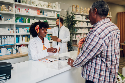 Portrait of an african american woman pharmacist assisting a senior customer while standing at the counter in a pharmacy. Customer Support in a drugstore. Copy space.