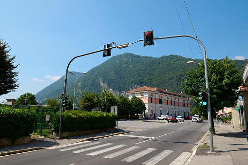 Pedestrian crossing, crosswalk and traffic light in the Italian town of Canso in Lombardy, with the Alps mountains in the background. Italy