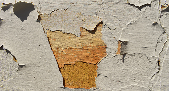 A weathered concrete wall, adorned with stains, cracks, and peeling white paint, showcases the intriguing beauty of urban decay and the passage of time.