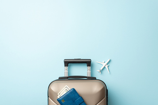 Your ticket to adventure. Top view of a miniature airplane, fashionable suitcase, and document wallet on a pastel blue backdrop, providing space for your text or ad