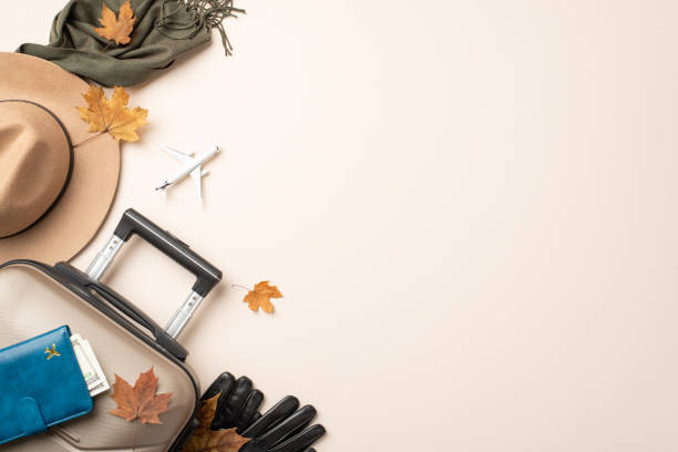 istock Autumn elegance during air travel. Top view of a mini plane model, chic essentials - floppy hat, cozy scarf, gloves, travel bag, documents wallet, fall foliage on neutral background 1717119085