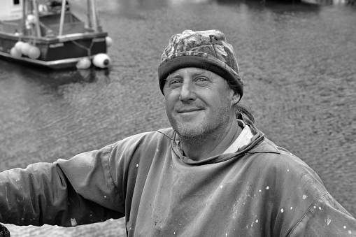Polperro, Cornwall, England, July 5th 2022: Black and white image of a friendly Cornish fisherman who has loaded his catch onto the jetty and is happy with his work for the day.