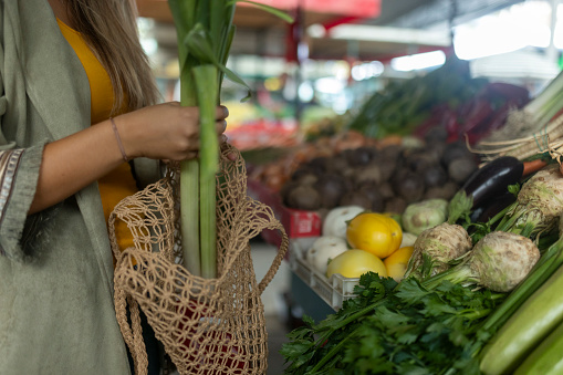 Close-up of the hands of an unrecognizable woman putting onions in a reusable bag while buying vegetables at the market