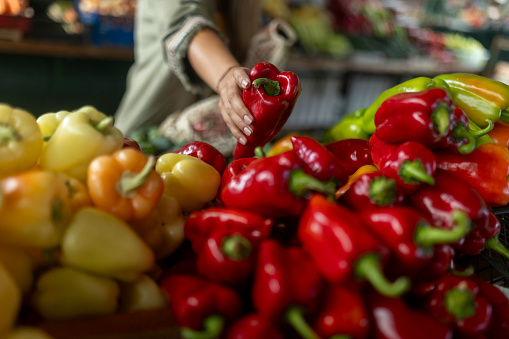 Close-up of the hands of an unrecognizable woman putting peppers in a reusable bag while buying vegetables at the market