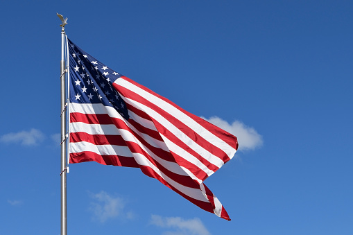 The USA flag, with its iconic red and white stripes and stars on a field of blue, set against a clear blue sky, symbolizing American patriotism and freedom.