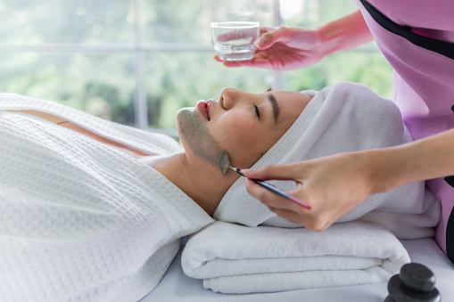 Side view of Asian woman lying down to getting face skincare treatment and therapy by facial masks from a professional beautician for skin health in spa salon. Young female with facial masks skincare.