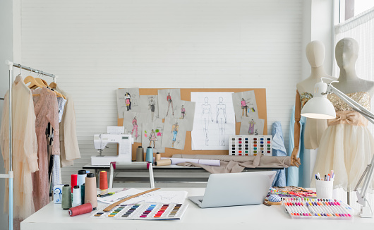 Workplace of designer dressmaker with dummy mannequin, sewing machine, laptop, thread, sketches, and equipment other in the fashion design studio office. Small business freelance startup concept.