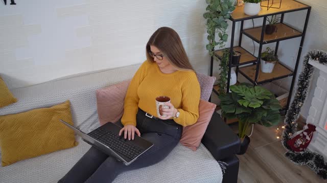 Young brunette woman using laptop and drinking coffee at home