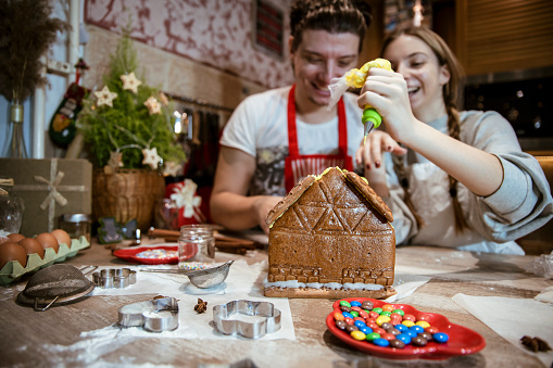 Teenage Brother and sister making Gingerbread house in the kitchen.