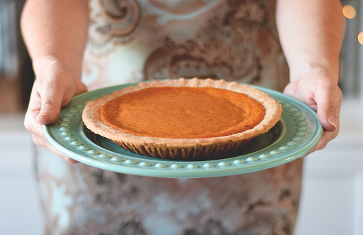 Woman's hands holding plate with pumpkin pie at Thanksgiving dinner