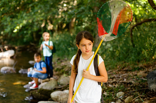 Little girl with net catching butterfly insects and learning about nature by the river