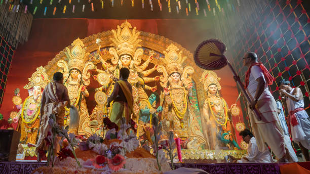 Hindu Purohits offering Vog, holy sweet food for Goddess Durga while worshipping her inside Durga puja pandal covered with holy smoke. stock photo