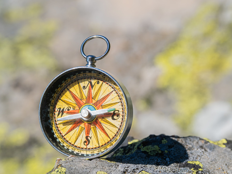 A compass is sitting on the sand, with the blue needle pointing to the north. The compass is surrounded by the ocean, creating a serene and peaceful atmosphere