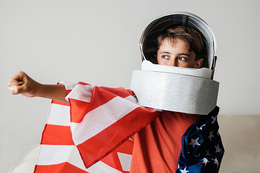 Astronaut kid playing with crafty helmet toy and wearing US American flag - Future spaceman dreaming and having fun at home