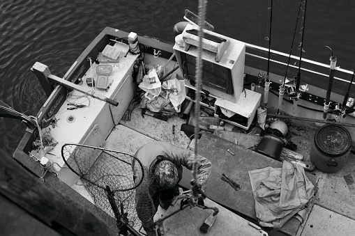 Polperro, Cornwall, England, July 5th 2022: Black and white image of a Cornish fisherman returning at low tide and getting ready to hoist his catch up to the jetty.