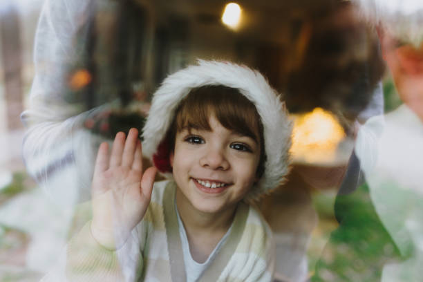 Photo of a little smiling boy sitting in front of a big window in a family home, waiting for a Santa Clause on Christmas Eve