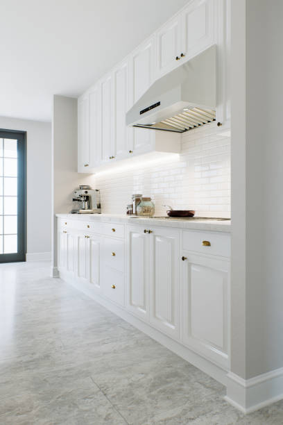 istock Kitchen with white cabinets, warm lighting and large metal hood. Kitchen interior with marble and brick tiles. 3d rendering. 1717263233