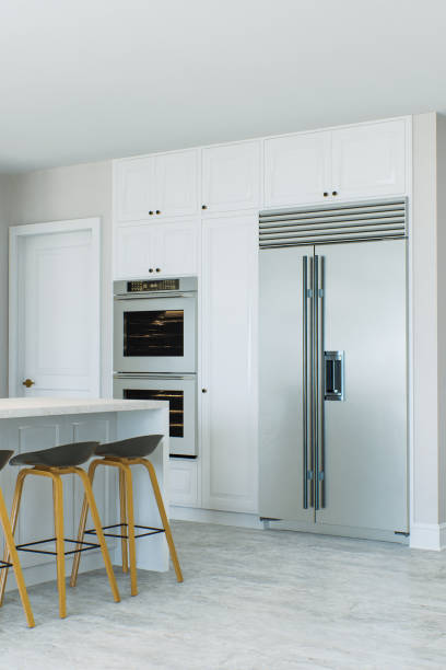 istock White kitchen with island, bar stools, refrigerator, built-in appliances. Bright kitchen with focus on large refrigerator. 3D rendering 1717263260