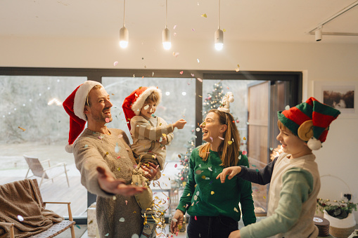 Photo of a family with two young children celebrating Christmas; throwing confetti and enjoying the lovely Christmas Eve together.