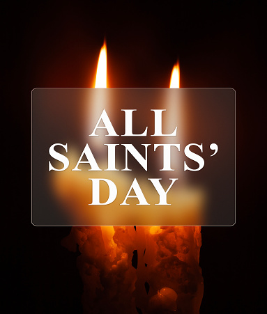 All Hallows' Day. Solemnity of All Saints. Two burning candles with blurred focus and text in glass frame.