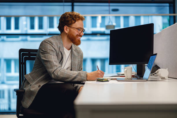 istock Handsome businessman working on laptop and making notes while sitting desk on office background 1717286002