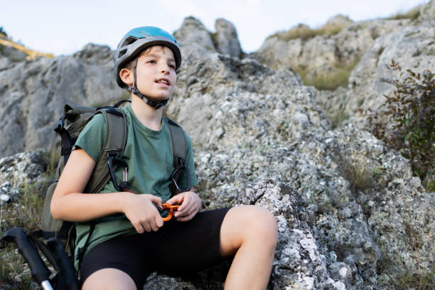 istock Young boy hiking in the mountains. He is using hiking equipment and wearing a backpack. Taking a break from the hard work. 1717295319