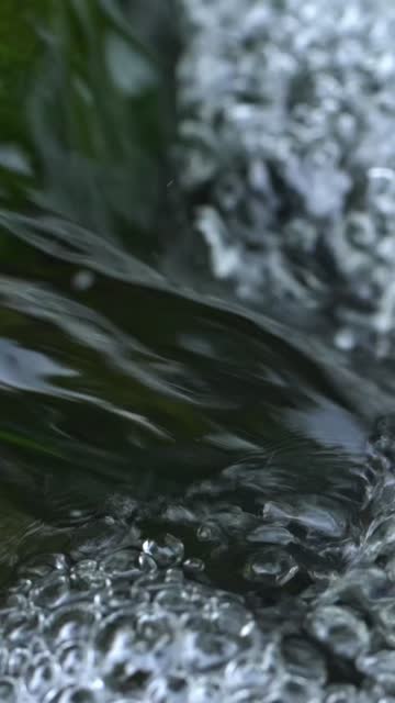 Close-Up of River Flowing over Green Moss-Covered Rock with Dancing Bubbles in Forest