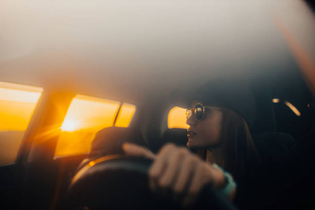 istock female driver in sunglasses and a baseball cap drives at sunset. 1717338499