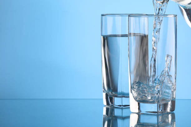 istock Pouring water into glass on light blue background. Space for text 1717382991