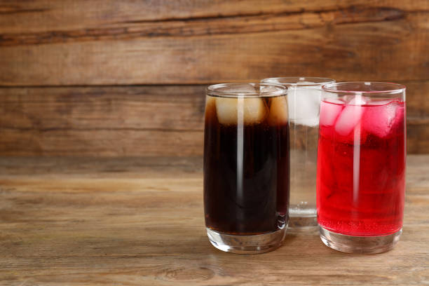 istock Glasses of different refreshing soda water with ice cubes on wooden table. Space for text 1717382995