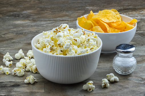 Close up of glass bowl full of popcorn against black background.