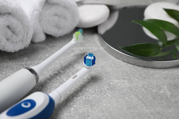 istock Electric toothbrushes, rolled towels and leaves on grey textured table, closeup. Space for text 1717399569