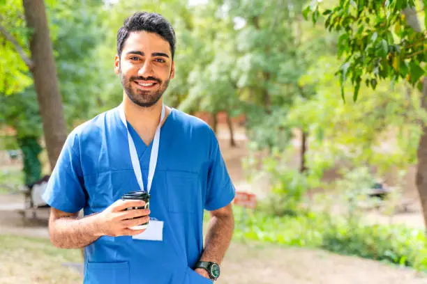 inturn in medical scrubs standing in the woods with a coffee cup