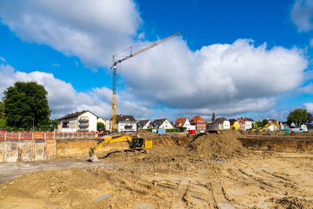 Excavation work on a construction site with excavators and tower crane.Residential area under blue sky with white clouds.
