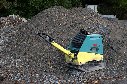 Vibratory plate compactor on a construction site next to a pile of gray gravel.
