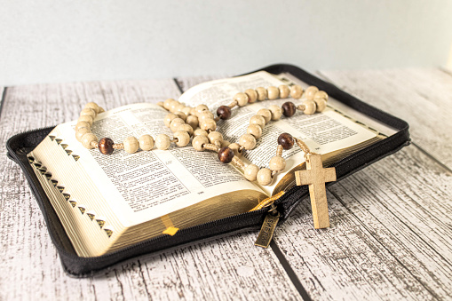 Rosary beads and crucifix cross on holy bible with candles in church.