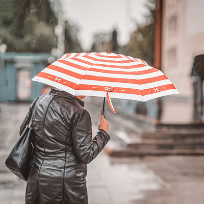 Rain. One elderly women under umbrella backs to us, lifestyle in the city