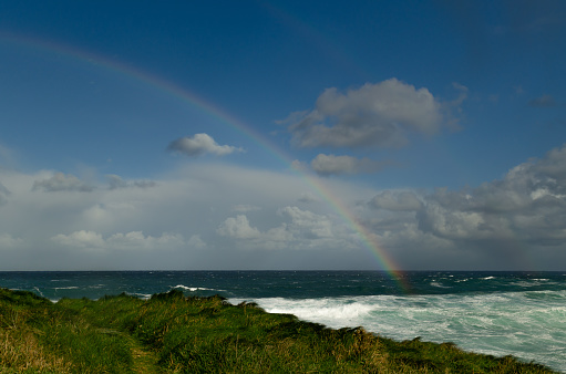 Wonderful turquoise blue sea with rainbows over the waves on a green coast of the Atlantic Ocean