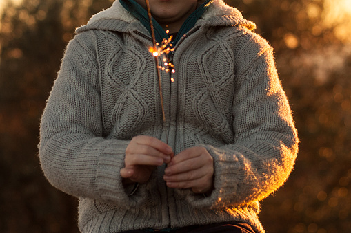 Child hands holding new year bengal. Sunny winter day. Sunset, Close up. Faceless, horizontal