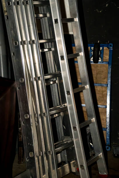 istock aluminum work ladders stored against a wall in a warehouse along with various work utensils. 1717505518