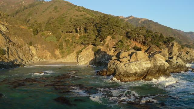 Aerial shot of Pfeiffer falls waterfall along the rugged coastline of Big Sur in golden afternoon light