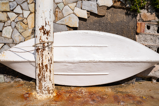 Small white wooden boat leaned on old wall in Agia Pelagia, Crete, Greece.