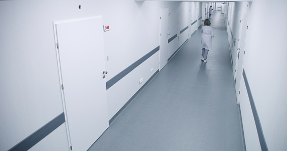 Hospital hallway: Busy doctors, professional medics, nurses, healthcare specialists walking. Operating rooms, clinic wards and offices. Medical personnel work in modern medical facility. High angle.
