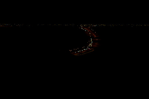 Photo shows Whoop-Up Drive in Lethbridge at night.  This is a curved stretch of roadway that takes traffic through the Oldman River Valley coulees, being the main fairway connecting the South and West sides of the city.  Photo is looking west, showing lights from businesses and homes on the west side, appearing in an ’s’ shape.