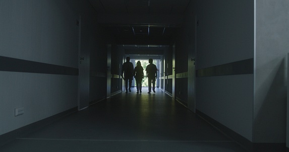 Following shot of doctors walking along the modern medical center corridor. Healthcare specialists and nurse enter the hospital room to patient or office. Medical staff in clinic hallway.