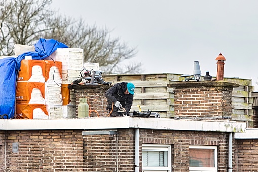Den Haag, Netherlands - January 06 2022: a roofer is on the roof of a home with a flat roof replacing it and placing isolation