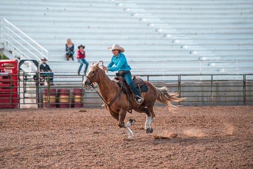 Cowgirl riding a horse in a rodeo arena. Barrel racing at a local competition.