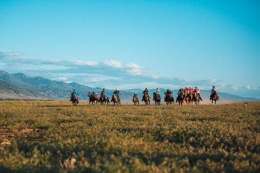 Outdoor shot of active cowboys and cowgirls having a blast together. They are horseback riding in the open field, their horses are running fast.
