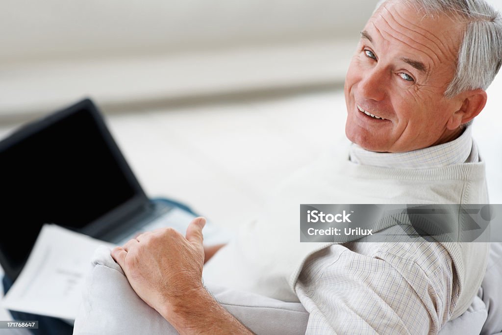Homme senior souriant à l'aide d'un ordinateur portable à la maison - Photo de Adulte libre de droits